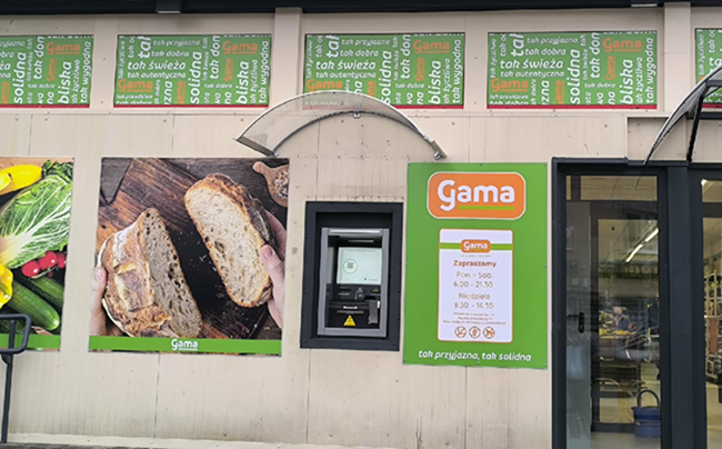 Zdjęcie przestawia nowy bankomat wbudowany w ścianę sklepu spożywczego